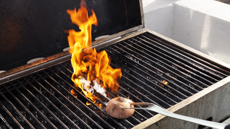 Grill flaming up as an onion on a grill fork is rubbed across it