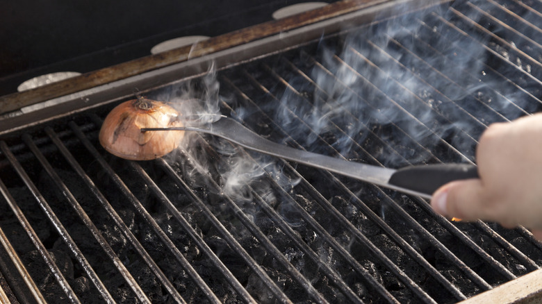 Someone uses a fork to rub an onion against the grates of a grill