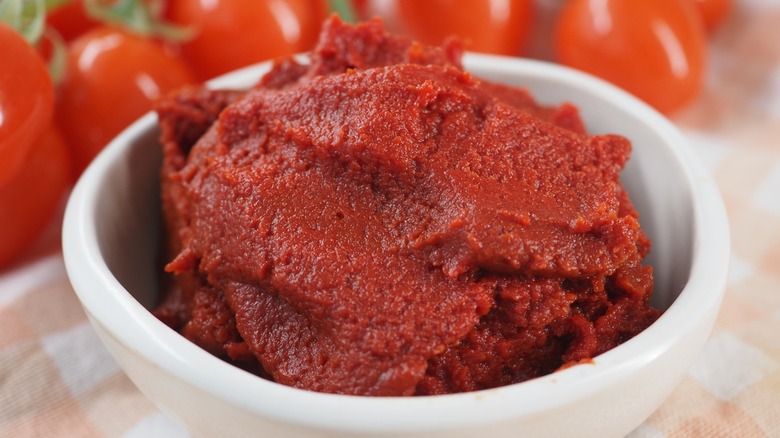 tomato paste in a white bowl with tomatoes blurred in the background