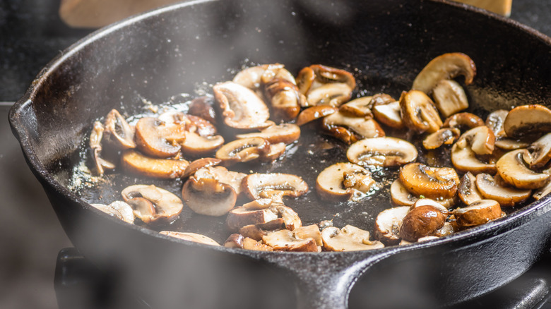 Sliced mushrooms being sautéd in a black cast-iron skillet.
