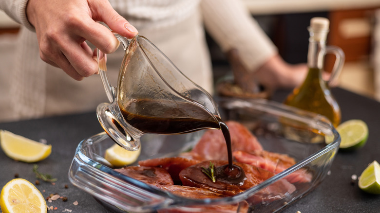 Person pouring sauce over glass pan of meat