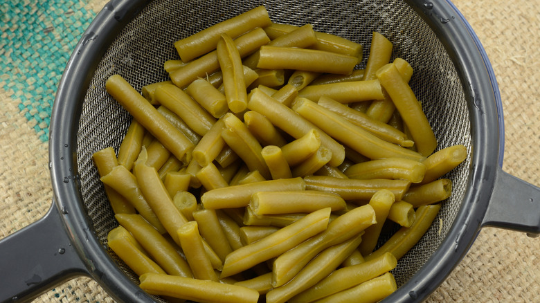 drained canned green beans in a sieve over a pan
