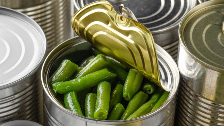 an open can of green beans surrounded by unlabeled closed cans
