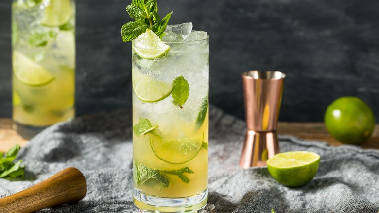 A Mojito next to limes and cocktail equipment
