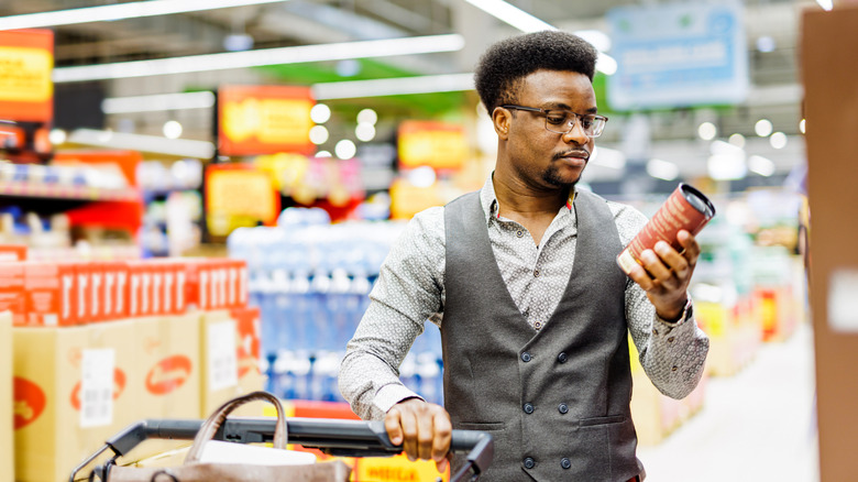A man wearing glasses and a vest reading the label on the side of a container