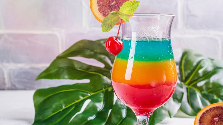 A colorful layered cocktail next to leaves and orange slices