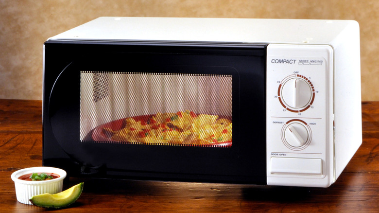 A plate of nachos in a white microwave, with salsa and a slice of avocado sitting in front