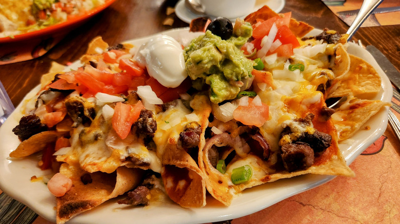 A heaping plate of restaurant nachos with sour cream, gaucamole, and salsa fresca