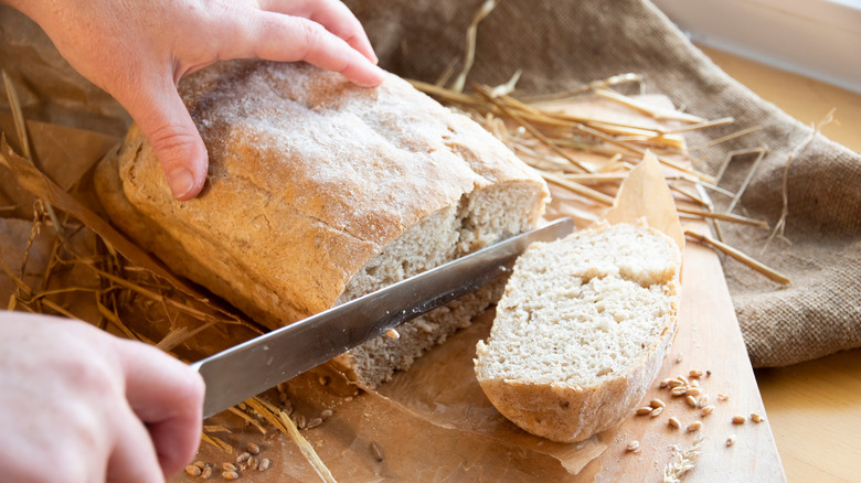 Hands slicing a loaf of homemade bread