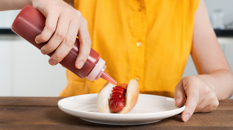 Hand squeezing ketchup onto hot dog