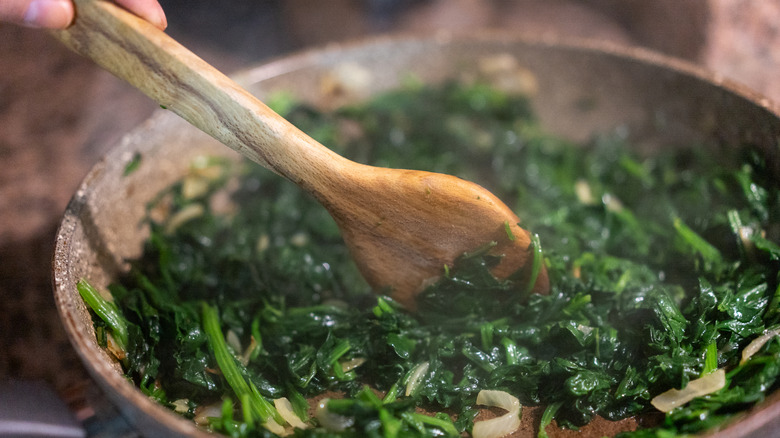 Cooking spinach in metal pan with wooden spoon