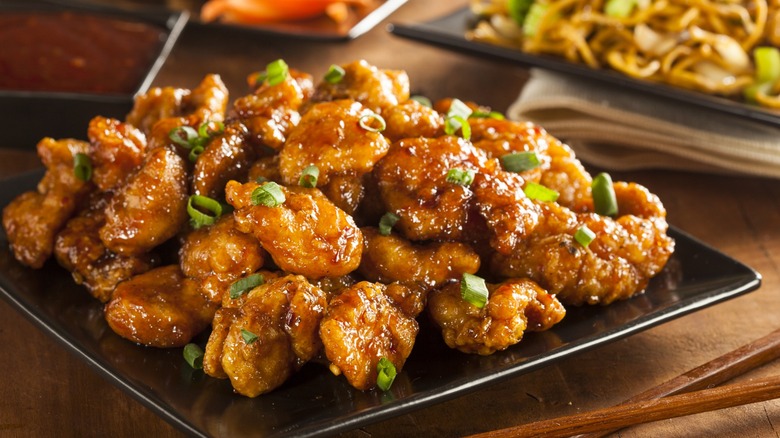 A black plate piled with orange chicken, sprinkled with green onion