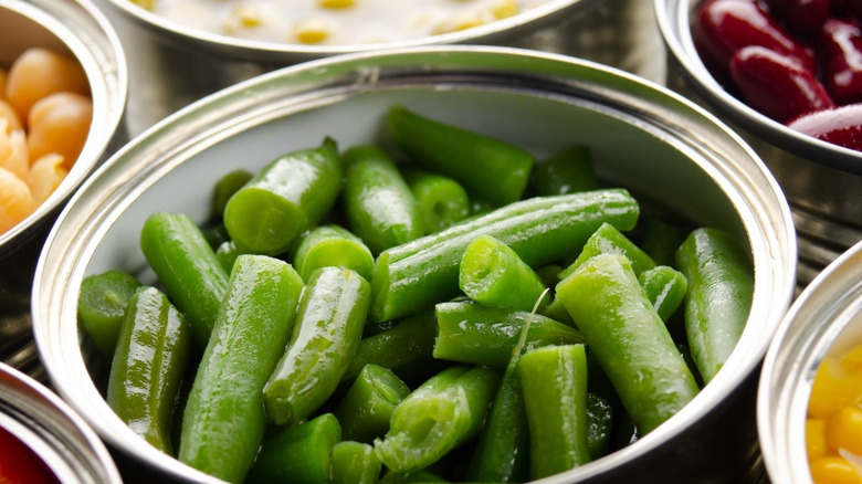 An open can of green beans, surrounded by other open cans of beans