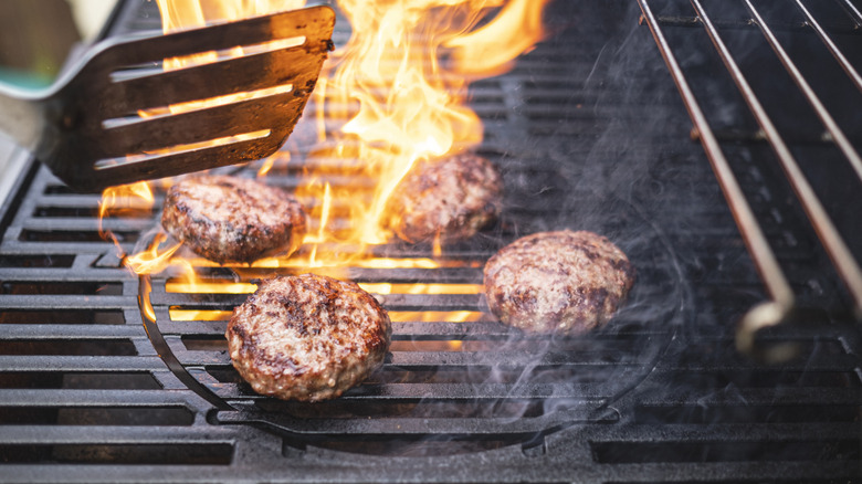 A spatula being held above some homemade hamburgers cooking on a grill