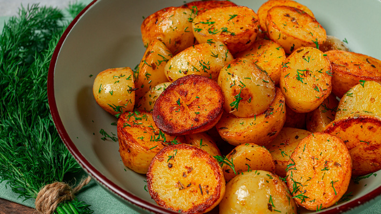A bowl of golden, crispy, roasted potatoes next to a bundle of fresh herbs.
