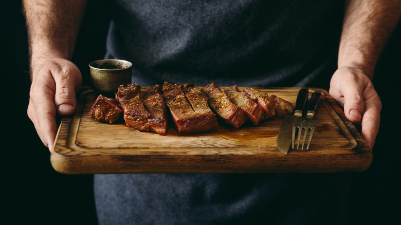 Hands holding steak on wooden board