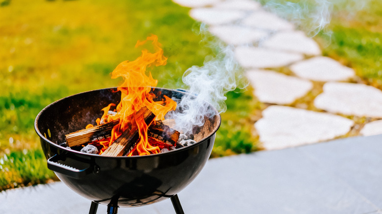 Black barbecue grill with stacks of wood on fire and smoking