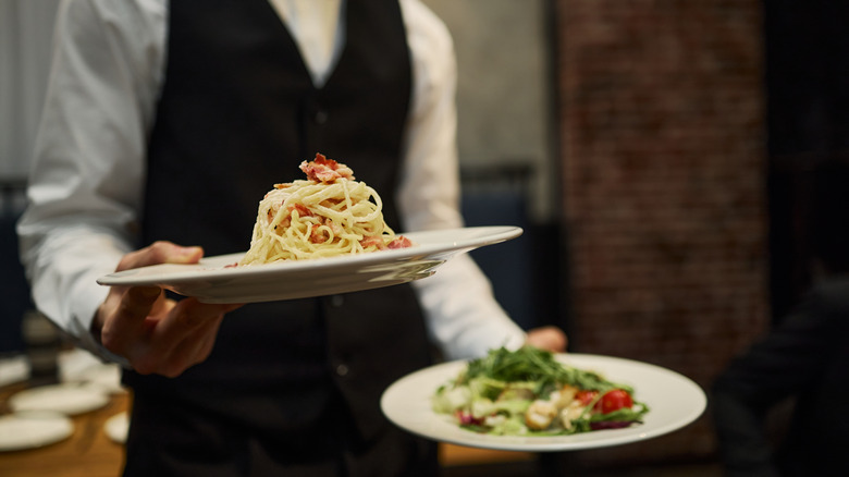 A formally dressed server holding two plates of food