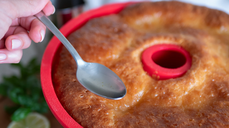 hand spooning rum syrup onto cake in red bundt pan