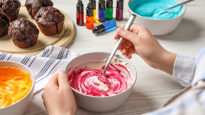 a woman stirs food coloring into frosting