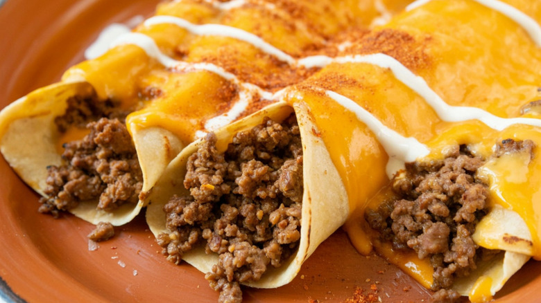 Ground beef taquitos with melted cheese and a sour cream drizzle