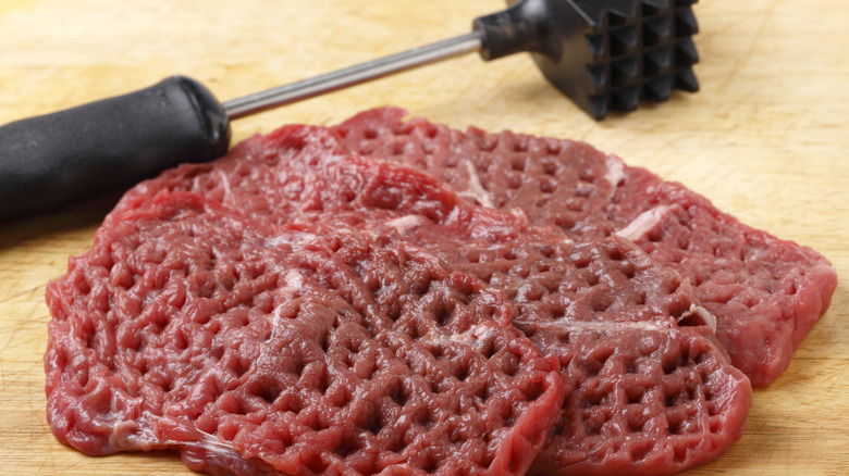 A very tenderized piece of steak with the dimpled mallet resting on a wooden cutting board