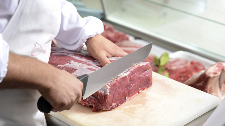 butcher cutting a slab of meat on a white board