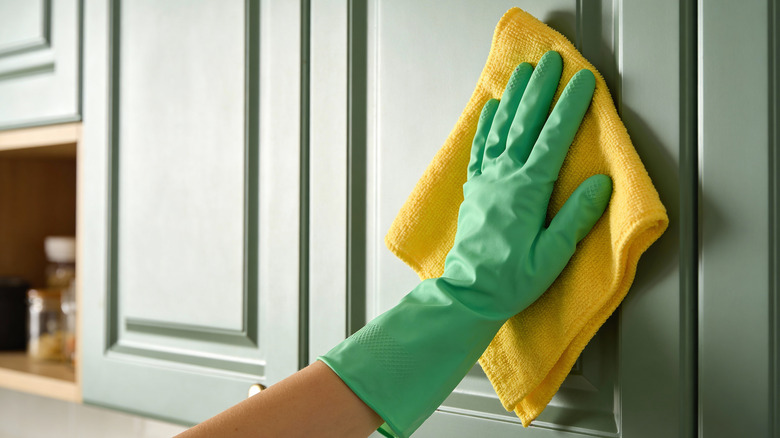 Hand in glove wiping green painted wood cabinet