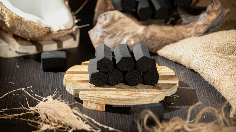 A small stack of coconut shell charcoal briquettes sitting on a wooden platter with coconut and burlap in the background