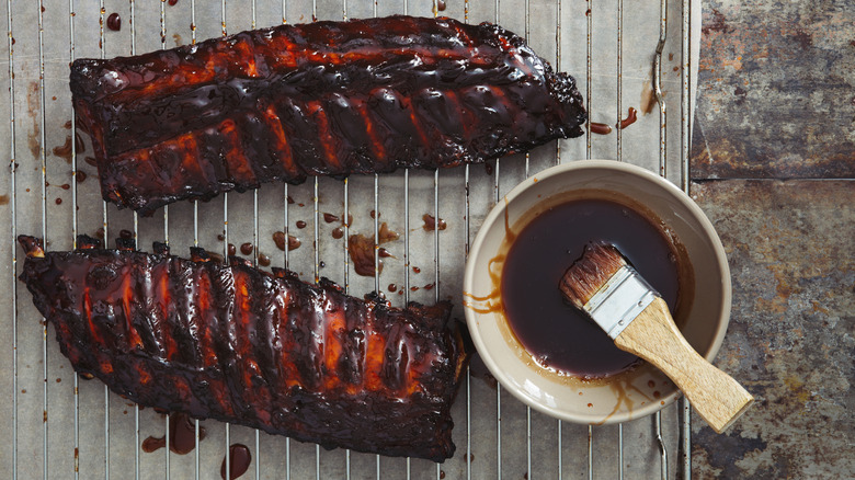 Cooked ribs on a rack beside barbecue sauce