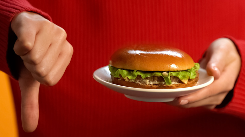 Someone holding a burger signaling thumbs down