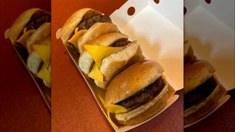 Three sliders with visible cheese and meat patties in the buns, sitting in a white box on a countertop