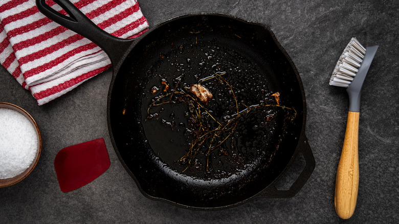 dirty cast iron skillet shown with coarse salt, a brush, and a cloth for cleaning purposes