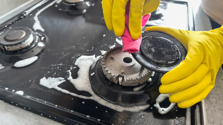gloved hands cleaning a gas stove's burner