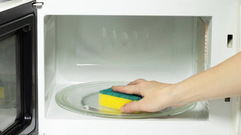 arm wiping out a newly-cleaned microwave oven with a scrubbing kitchen sponge