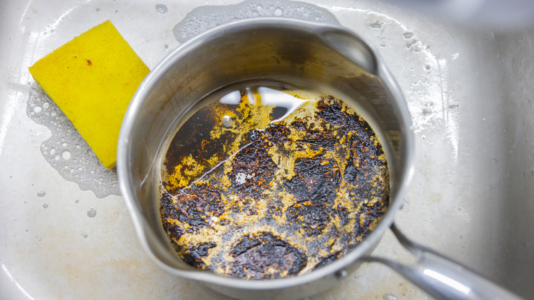 Saucepan in sink with burned-on food next to kitchen sponge