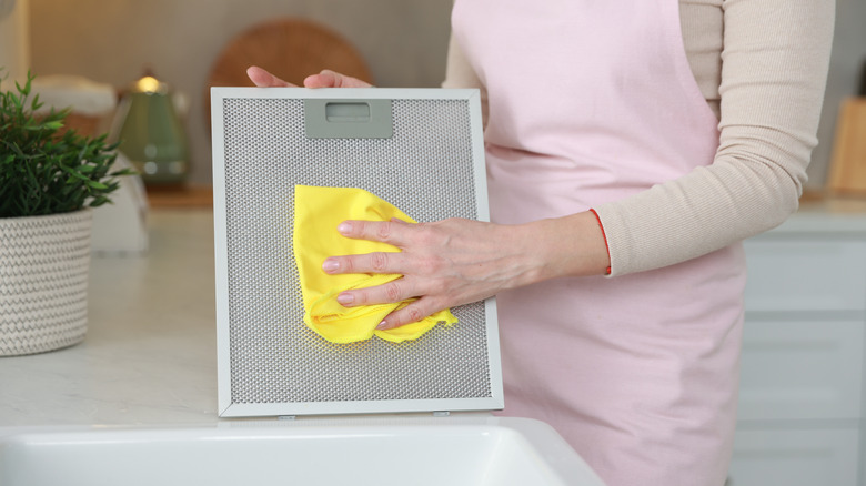 person in a pink apron drying a clean range hood filter with a soft cloth beside the sink
