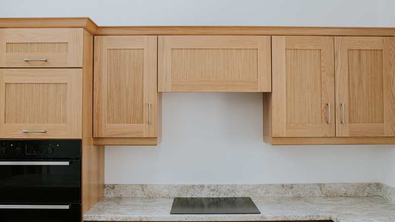 A set of somewhat dated upper kitchen cabinets with a wood finish over a stone counter with a small cooktop