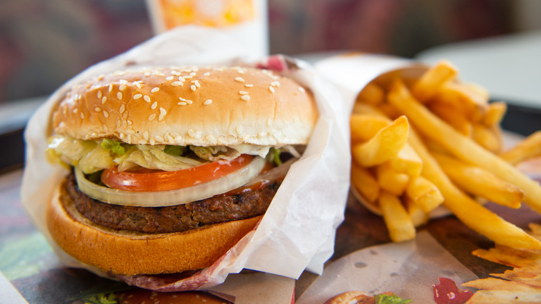 Burger King Whopper burger in paper wrapping next to sleeve of French fries on tray