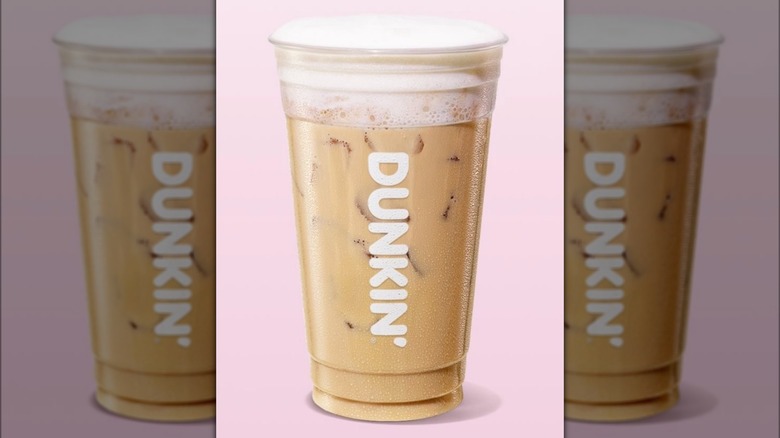 Clear plastic cup of Dunkin' Dirty Soda beverage against pale pink background