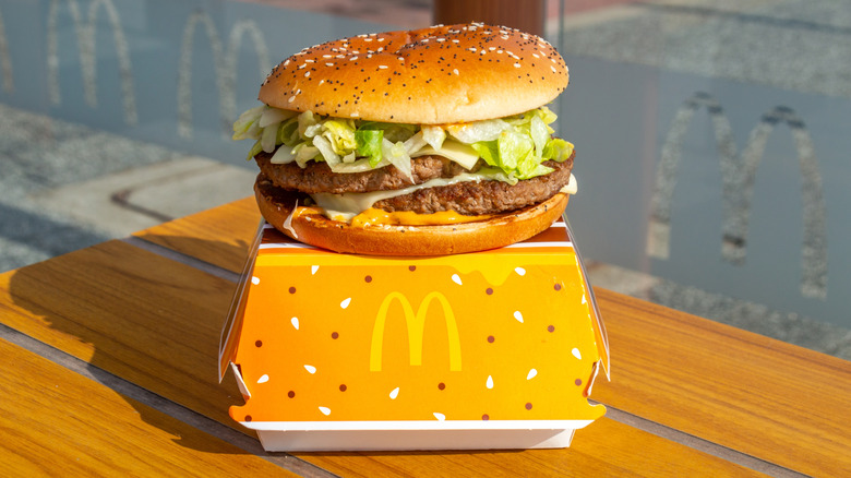McDonald's Big Arch burger sitting on top of yellow cardboard box with McDonald's logo on wooden table