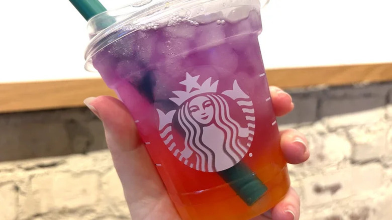 a hand holding a plastic cup of Starbucks Toprical Butterfly Refresher with a large green straw in it