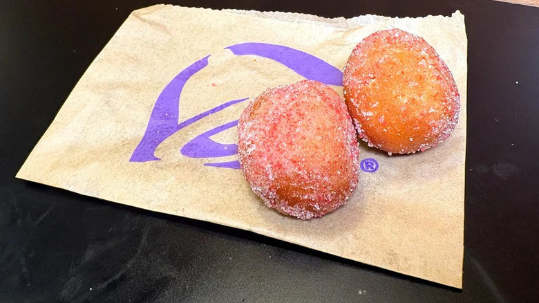 Two Taco Bell Strawberry Cinnabon Delights sitting atop thir paper bag on a black surface