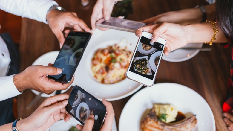 Group of people taking photos of their meals on a restaurant table