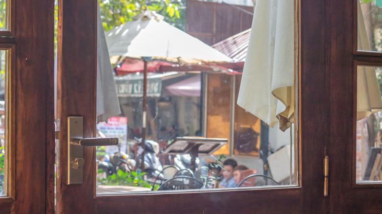 A close-up of a large, wooden door in a restaurant with a glass window view to patio seating outside