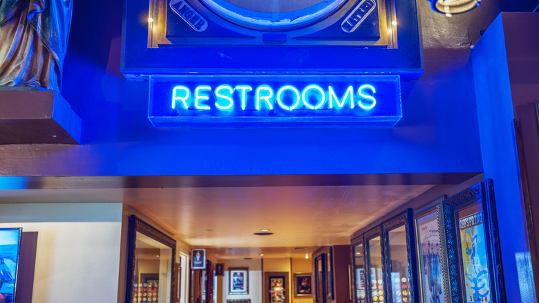 A glowing neon "restrooms" sign above a doorway in a flashy restaurant