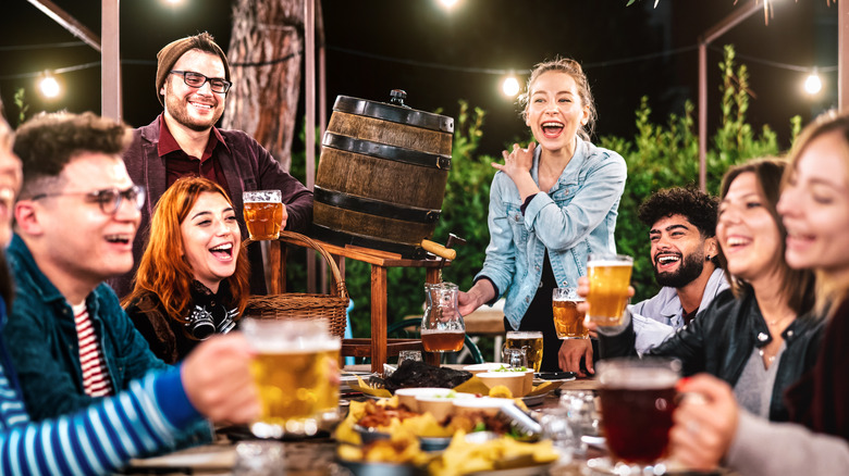 A large, raucous group of friends holding beer mugs around a table at a restaurant