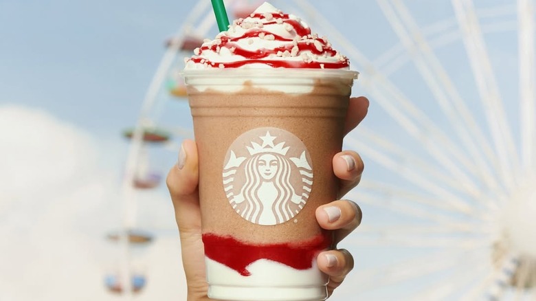 Hand holding a Strawberry Funnel Cake Frappuccino in front of Ferris wheel