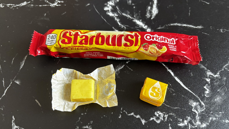 A sealed package of Starburst original flavor with both a wrapped and unwrapped lemon Starburst in front of it