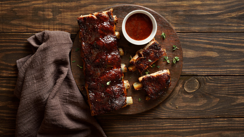Rack of BBQ ribs on wooden board and wooden table with cup of sauce